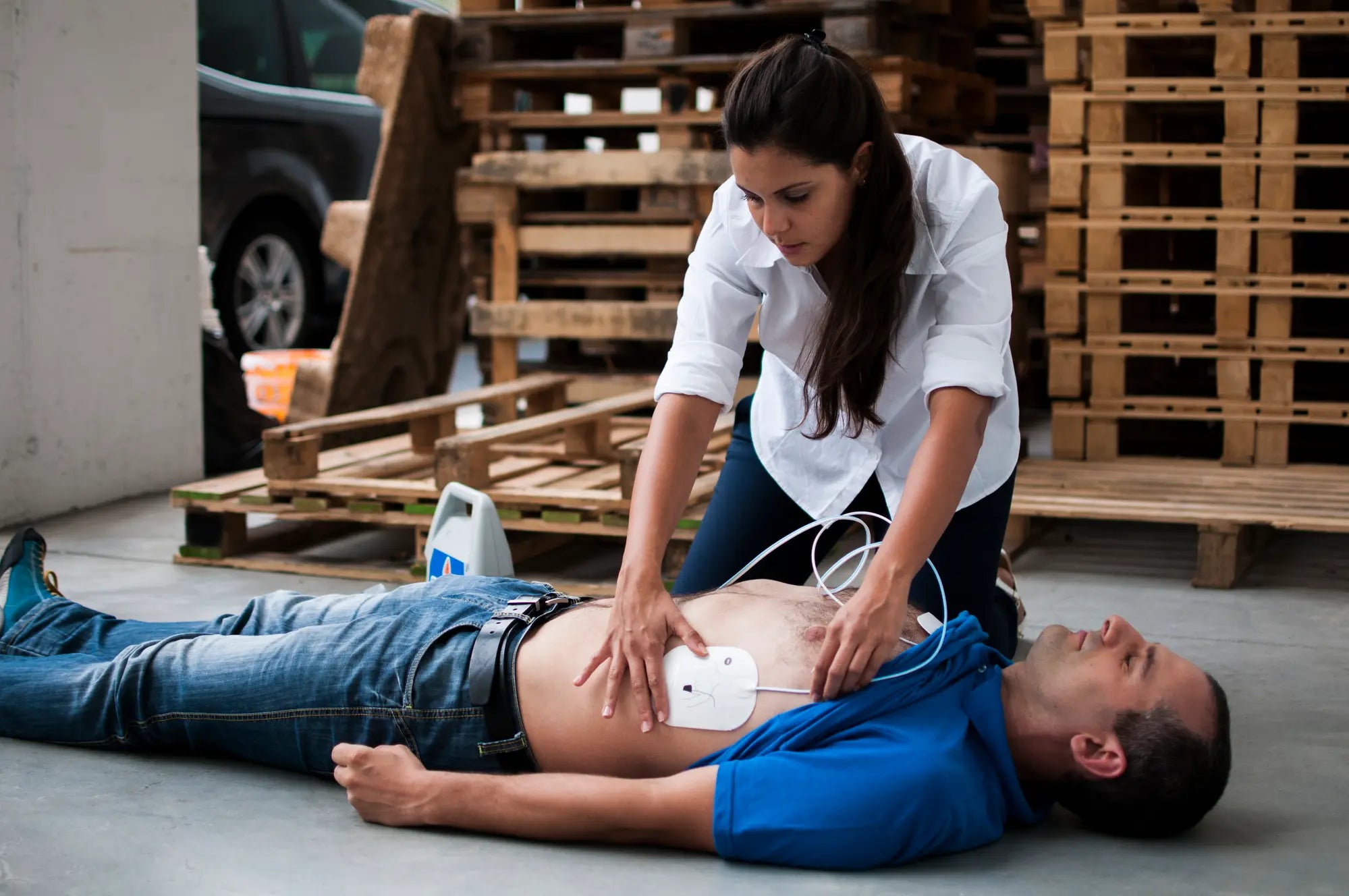 A woman applying electrode pads to a man who has fallen victim to sudden cardiac arrest
