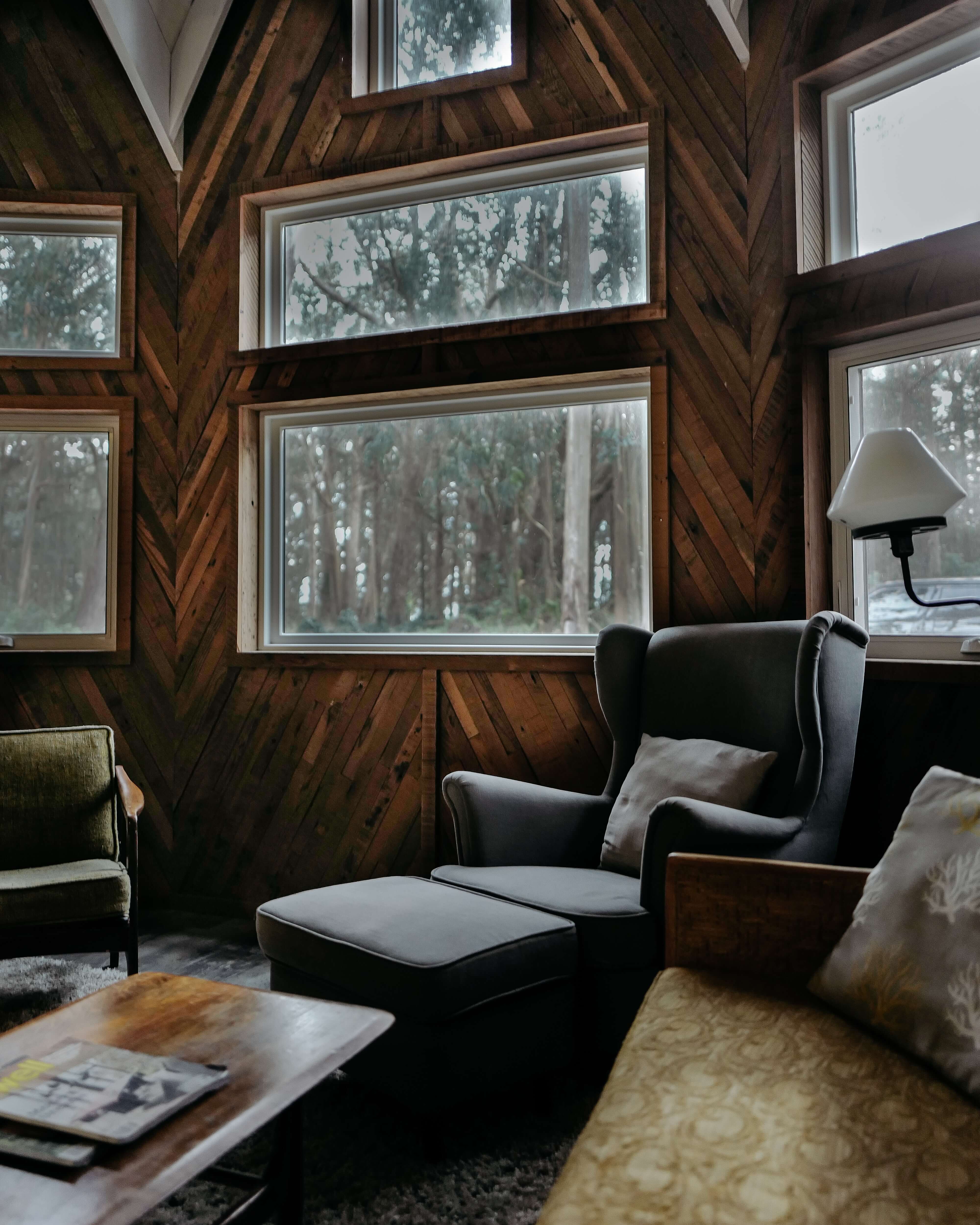 A cabin style living room with big windows and comfortable furniture