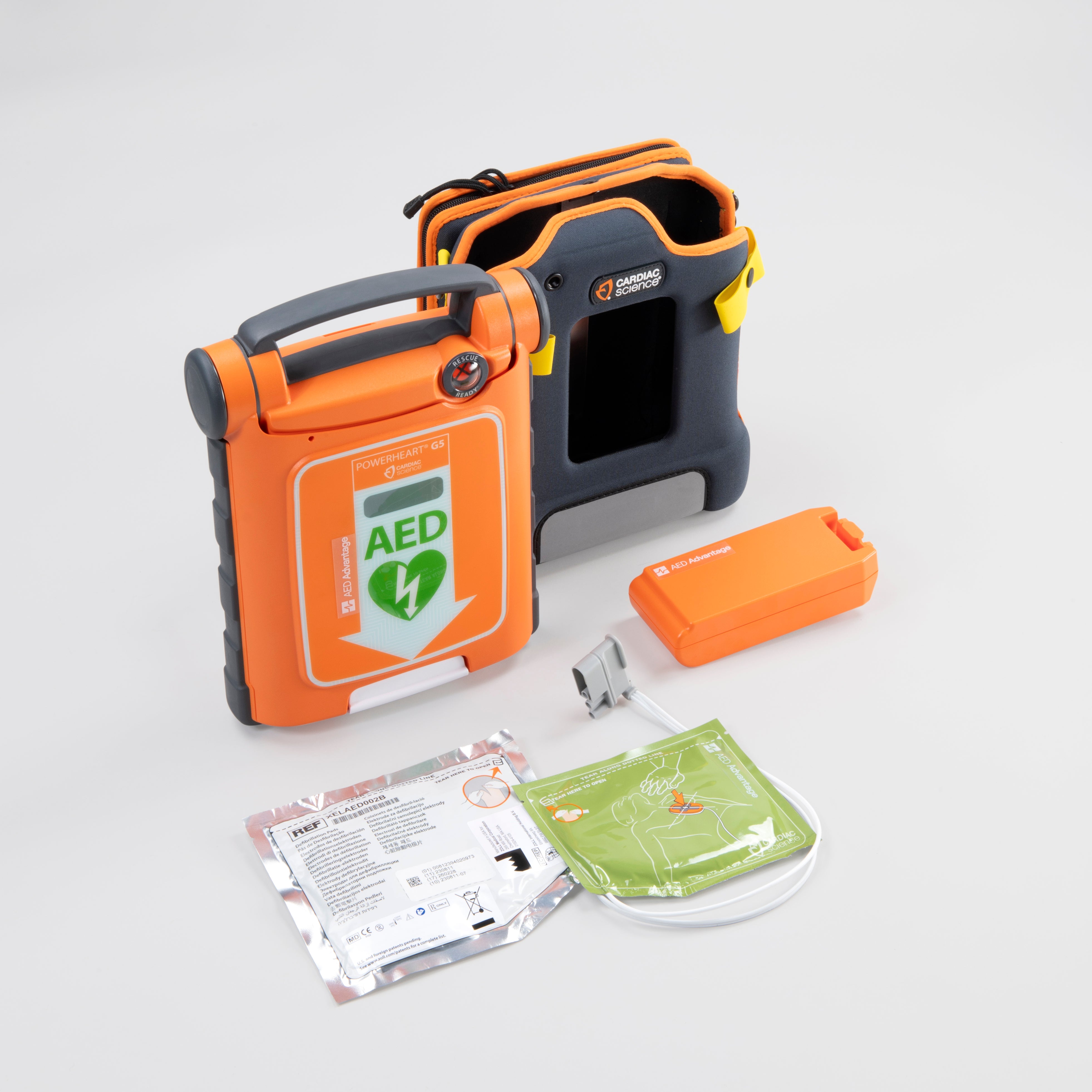 An orange Powerheart G5 AED displayed with its carry case, electrodes, and battery