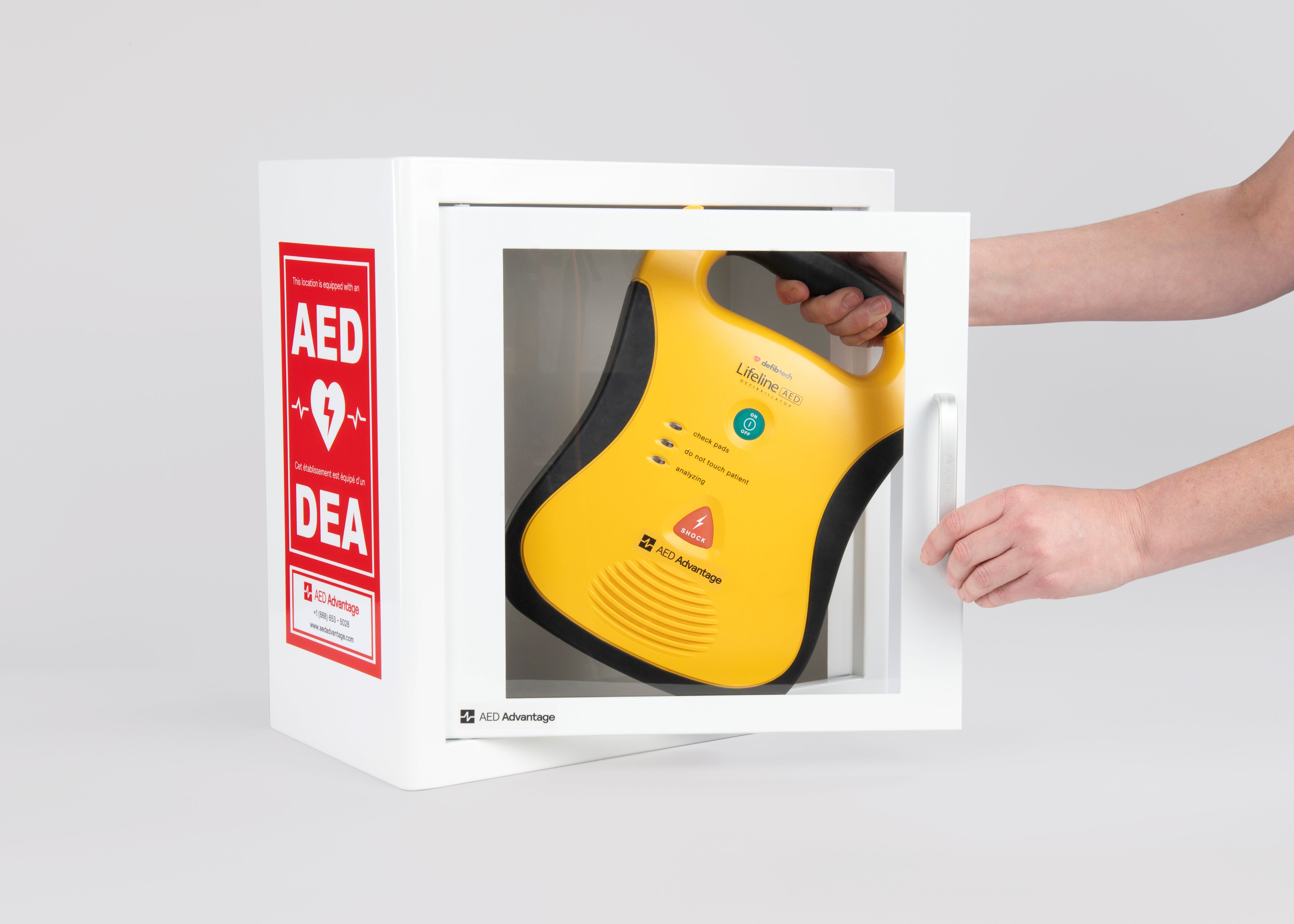 A yellow and black Defibtech Lifeline AED being retrieved by hand from a white metal cabinet with red decals