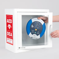 A blue and white HeartSine AED being retrieved by hand from a white metal cabinet with red decals