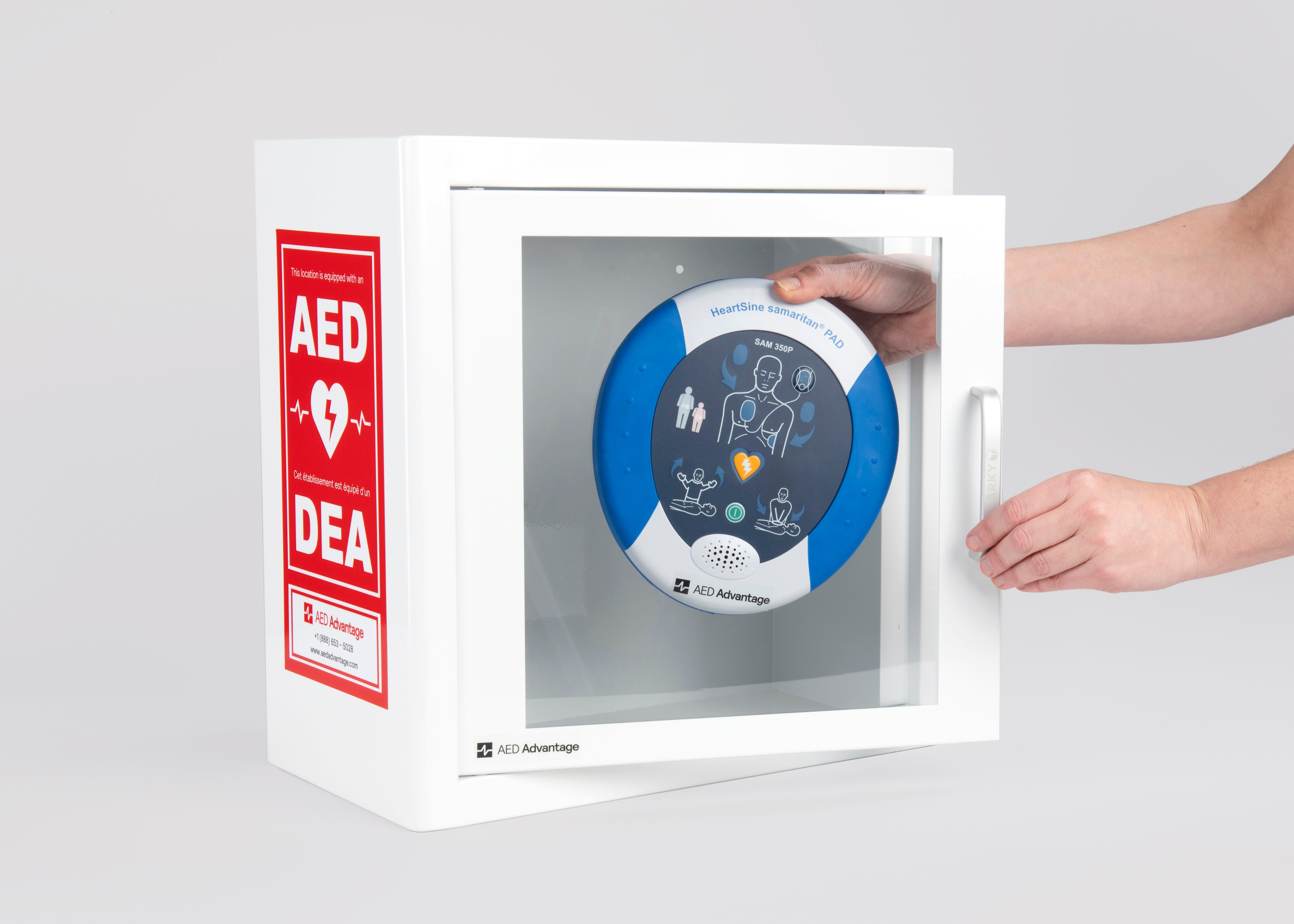 A blue and white HeartSine AED being retrieved by hand from a white metal cabinet with red decals