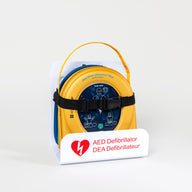 A HeartSine 360P AED in its yellow carry case strapped into a white wall mount bracket