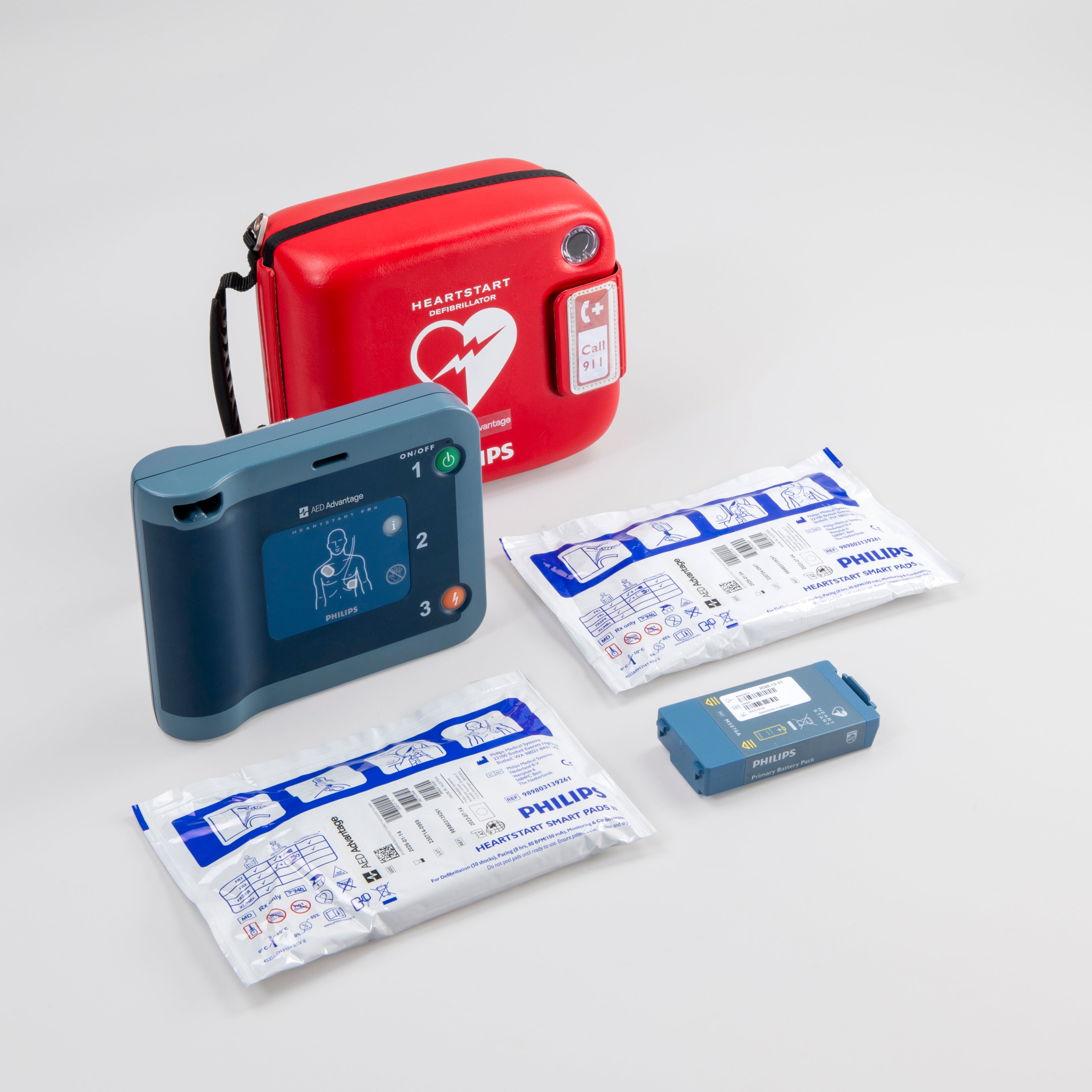 A blue Philips FRx AED displayed with its red carry case, two electrode pads, and a battery