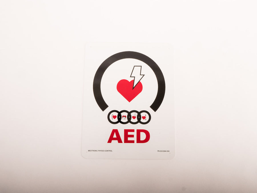 A white universal AED wall mount bracket with black straps and red signage